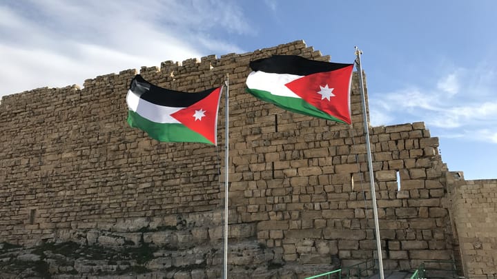 Two Jordanian flags on an old stone fortress wall