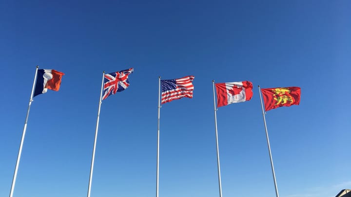 The flags of France, the UK, the US, Canada and Normandy on flagpoles against a blue sky
