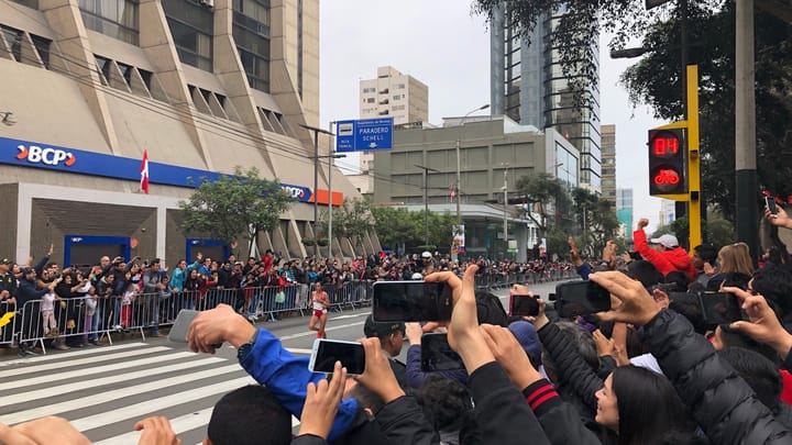 A crowd holding up phones to film a parade on a street in Lima